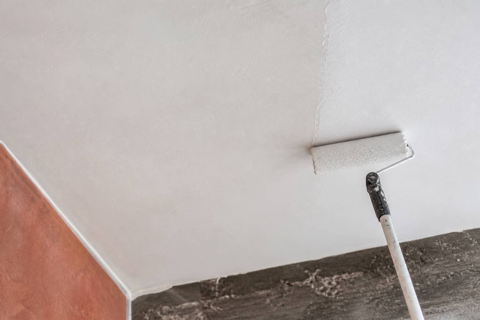 Rouleau et bac à peinture posés sur une bâche pour peindre un plafond