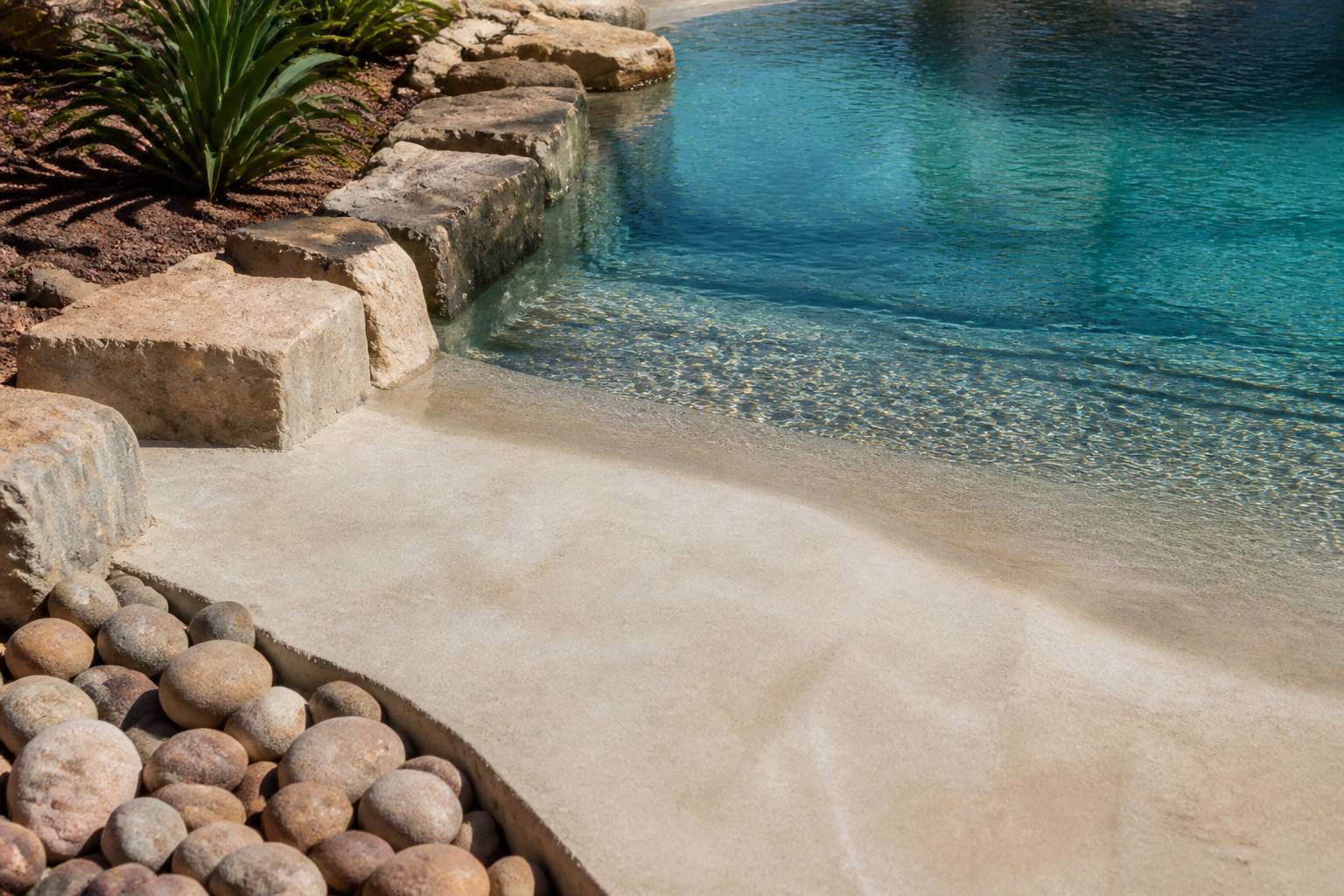 Rebord en pierre naturelle et plage en pente douce d'une piscine lagon